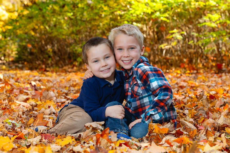 Two brothers play in autumn leaves while taking a family portrait photo at the Dominion Arboretum in Ottawa