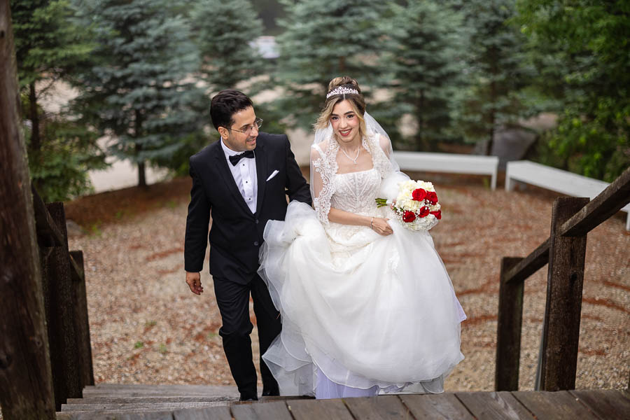 With light rain overhead, a groom supports his bride as they walk up a flight of stairs at Le Belvedere.