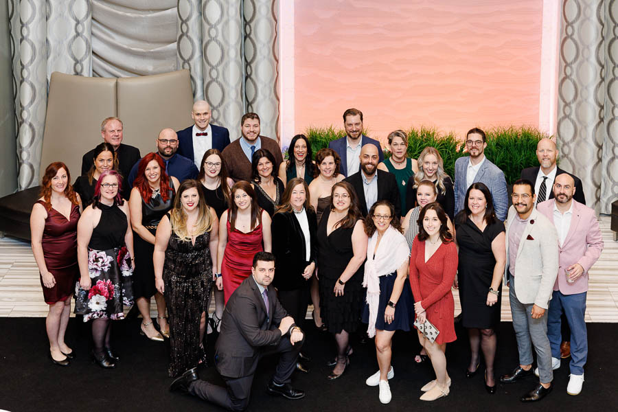 A large team photo taken during a corporate event at the Infinity Convention Centre in Ottawa.